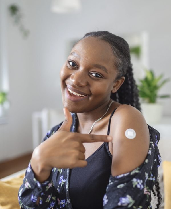 Portrait of a female smiling after getting a vaccine. Woman holding down her shirt sleeve and showing her arm with bandage after receiving vaccination.