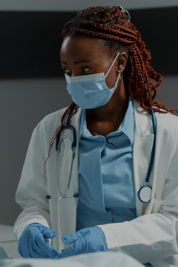 Recovering patient in hospital ward getting consultation from african american doctor with face mask and stethoscope. Elder man with nasal oxygen tube and oximeter sitting in bed